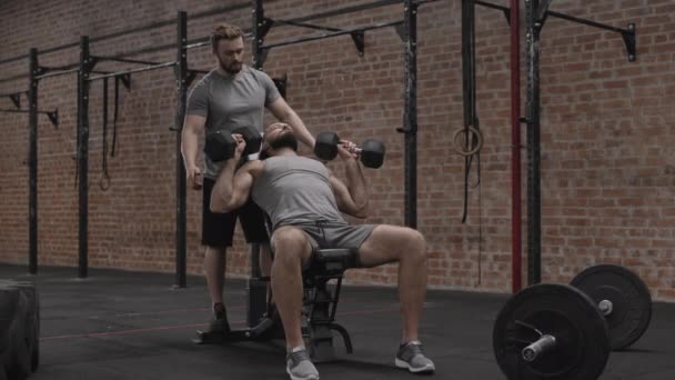 全景肌肉健身教练身穿运动服 帮助英俊的白种人提起哑铃 伸展背部肌肉 — 图库视频影像