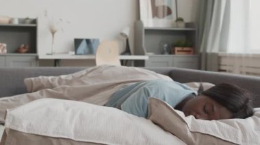 Pijama giymiş genç Afrikalı kadın portresi. Yatakta yatıyor, uyuyor. Sonra uyanıyor, kameraya bakıyor ve gülümsüyor.