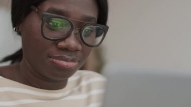 Gözlüklü genç Afro-Amerikalı iş kadını bilgisayar ekranına bakıyor.