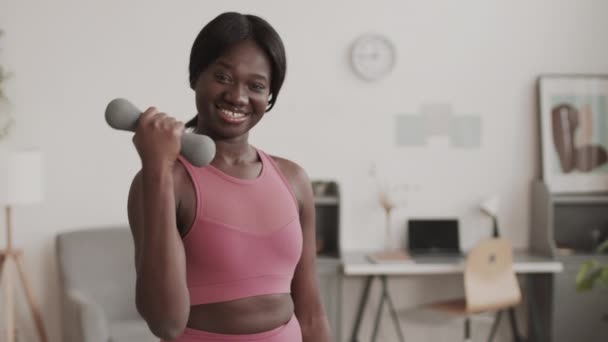 身穿时髦运动服的年轻非洲裔美国女运动员在客厅里用哑铃做运动 面带微笑地看着镜头的自画像 — 图库视频影像