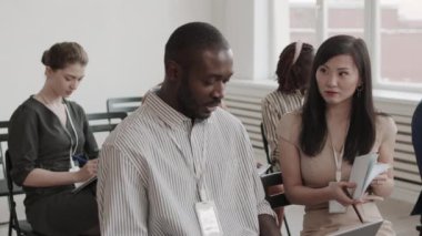 Orta boy Asyalı bir kadın ve Afrikalı bir adamın konferans odasında oturup gülümseyişlerinin fotoğrafı.