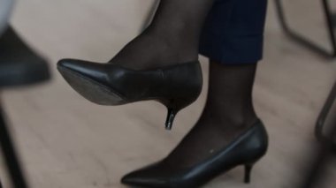 Yakın plan. Takım elbise, tayt ve siyah topuklu ayakkabı giyen, sallanan bacağı olan, tanınmayacak hale gelmiş, tanınmamış bir insan.