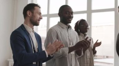 Odada ayakta alkışlayan, gülümseyen, beyaz ve Afrikalı erkeklerin el sıkıştığı orta ışıklandırılmış mutlu iş arkadaşları.