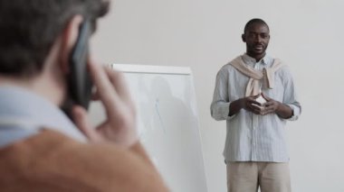 Afrika erkek yöneticisinin omuz hizasında, beyaz tahtanın yanında dikilip, grafikle konuşuyor, sonra da cep telefonuyla konuşan tanınmayan bir meslektaşa odaklanıyor.
