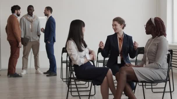 アフリカ人 アジア人の女性の同僚の中長い話 ホワイトボードの近くに立っている男性の同僚の前で会議室の椅子に座って — ストック動画