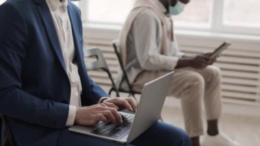 Mavi takım elbiseli tanınmayan bir iş adamı konferans odasında bulanık iş arkadaşından uzakta oturuyor, dizüstü bilgisayarın klavyesinde daktilo yazıyor.