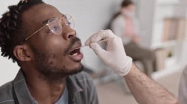 Yüksek açılı yakından çekilmiş tıbbi eldiven, tanınmayan bir tıp işçisinden tükürük örneği, hastanedeki Afrikalı bir adamın ağzından pamuk örneği alıyor.