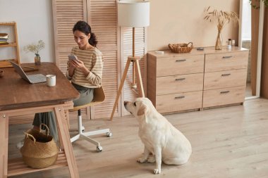 Geniş açılı modern kadın portresi. Ev telefonuyla ev telefonu kullanıyor. Yanında köpek oturuyor.