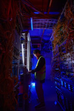 İnternet bağlantısı kurarken sunucu odasında dizüstü bilgisayar kullanan genç ağ teknisyeninin gelecekteki yan görüntüsü
