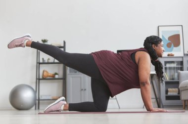 Kıvrımlı Afrikalı Amerikalı kadın evinde çalışıyor yoga minderine uzanırken gülümsüyor, boşluğu kopyalıyor.