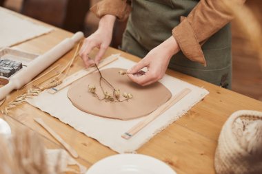 Çömlekçilik atölyesindeki ahşap masaya bitki damgalı seramik yapan tanınmamış kadın zanaatkârların yakın plan fotoğrafları.