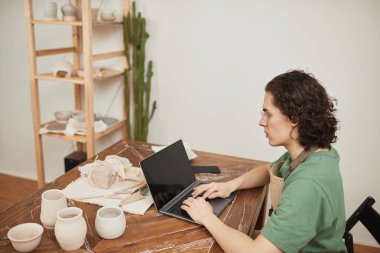 Küçük işletmeleri yönetirken atölyede dizüstü bilgisayar kullanan genç adamın yan görünüm portresi, boşluğu kopyala