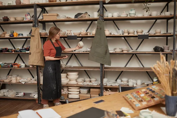 stock image Background image of young female artisan organizing ceramics on shelves in pottery workshop, copy space