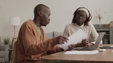 Orta boy Afrikalı bir kadın elinde belgelerle masada oturuyor ve genç bir Afro-Amerikalı adamla iletişim kuruyor. Yanında oturuyor ve dizüstü bilgisayarda klavye kullanıyor.