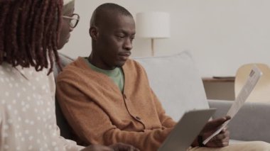 Genç Afrikalı kadın ve adamın oturma odasında kanepede oturup evrak işleriyle uğraşması. Laptop klavyesinde yazan kadın