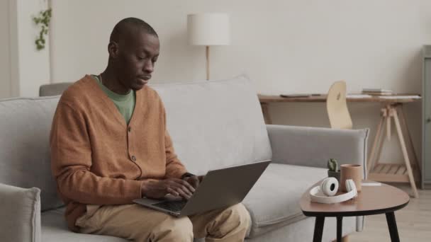 Середній Постріл Молодого Лисого Африканця Повсякденному Одязі Сидячи Дивані Ноутбуком — стокове відео