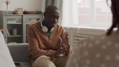 Kel ve genç Afrikalı bir adamın ensesinde günlük giysiler ve kulaklıklar vardı. Kanepede oturuyordu ve tanınmayan kadın psikologla konuşuyordu.