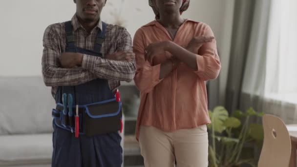 彼らの胸の上にカメラと交差腕を見て リビングルームに立っている制服と若いアフリカの女性を身に着けている若いアフリカ系アメリカ人男性の参加者の傾き — ストック動画
