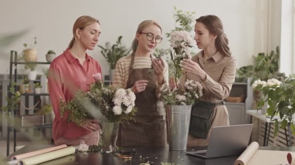 三个白人女花匠 中等身材 站在花店柜台后面笑着 看着花瓶里的花 讨论花束的设计和排列 — 图库视频影像