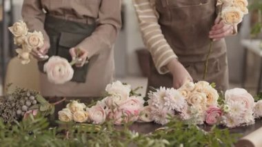 İki tanınmayan çiçekçi masasında durmuş, taze gülleri ve kasımpatıları ayırıyor.