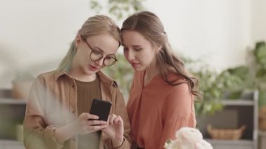 Akıllı telefona bakan, konuşan, içeride gülen iki genç beyaz kadının belinden yukarı doğru.