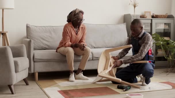 帮助非洲裔美国妇女组装新木椅的非洲男性专业家具组装工人的全景 — 图库视频影像