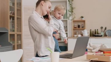 Genç, meşgul, beyaz bir annenin bebek taşıması, evdeki sandalyeye oturması, telefon görüşmesi yapması, dizüstü bilgisayar kullanması, çocuğun gitmesine izin vermesi.