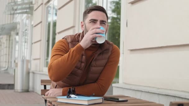 스웨터와 조끼를 테이블에 스마트폰 이어폰을 컵에서 커피를 마시고 남성이 일어나고 — 비디오