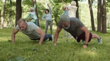 Diğer insanlar arka planda ısınırken, iki beyaz sporcunun parkta şınav çekerken geniş açılı görüntüsü.