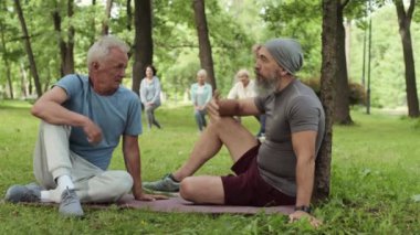 Açık havada çimenlikte lastik hasırın üzerinde spor giyip, spor yapmaya başlamadan önce iletişim kuran iki Kafkas sporcusunun geniş açılı görüntüsü.