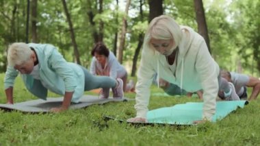 Bir grup yaşlı sporcu açık hava antrenmanı sırasında parkta lastik minderlere şınav çekiyorlar.
