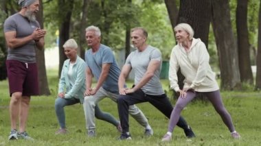 Yakışıklı, yaşlı, sakallı antrenör onları izlerken dört yaşlı sporcu grubu parkta ileri doğru hamle yapıyor.