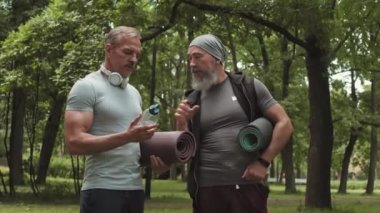 Parkta antrenmandan önce iki yakışıklı beyaz sporcunun sohbet ederken orta boy fotoğrafı. Sonra yaşlı sporcu kadın geliyor ve onları selamlıyor.