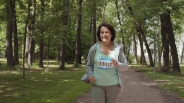 Orta yaşlı aktif kadın koşucunun spor giysileri içinde parkta maraton koşarken çekilmiş bir fotoğrafı.