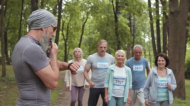 Spor giyimli beyaz erkek ve kadınların yakışıklı sakallı erkek koçun ıslık çalmasından sonra parkta koşarken çekilmiş birkaç fotoğrafı.