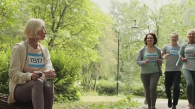 Tahta kütüğün üzerinde oturan, dinlenen ve içme suyu içen sarışın beyaz bir kadın sürüsü. Sonra da ormanda koşan bir grup sporcuya katılıyorlar.