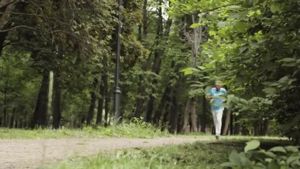 穿着运动服和运动鞋在森林里跑步的老年白人男性运动员的全景 — 图库视频影像