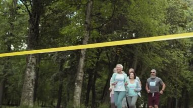Birkaç yaşlı sporcu erkek ve kadının açık havada maraton koşarken çekilen fotoğrafları. Kısa saç kesimi olan yaşlı sporcu kadın bitiş çizgisini geçip yarışı kazanıyor.