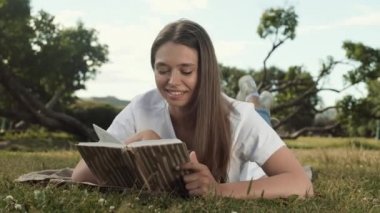 Yeşil çimlerin üzerinde yüzüstü uzanmış, komik kitaplar okuyan, gülen, sonra da kameraya bakan mutlu beyaz kadının sol bakış açısını izlemek.