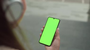Elinde yeşil ekranlı cep telefonu tutan tanınmayan birinin omzundan. 