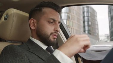 Resmi kıyafetler giyen, arabada oturan ve evrakları dikkatle inceleyen endişeli genç işadamlarının sandığı.