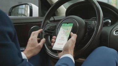 Kesilmiş tanınmayan araba sürücüsü sabit lüks bir otomobilde direksiyonda oturuyor, akıllı telefonda online harita uygulaması kullanıyor.
