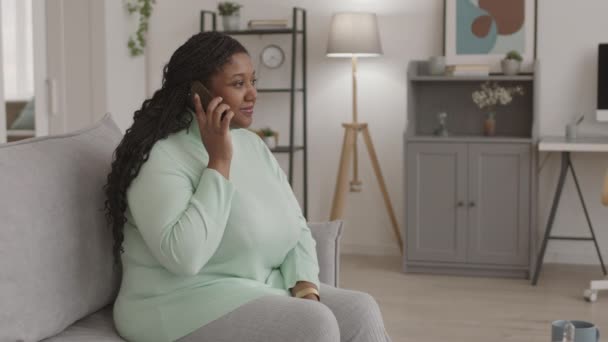 若いアフリカ系アメリカ人の女性の中には 自宅でソファに座って電話で話すカジュアルな服を着て — ストック動画