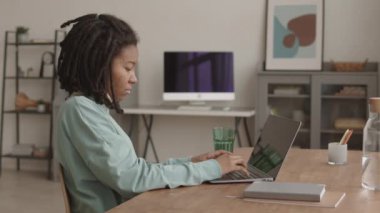 Orta boy Afro-Amerikalı bir kadın. Cildi sorunlu ve şık kıyafetler giymiş. Masaüstü bilgisayarı başında oturuyor ve ödevlerini yapıyor.