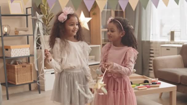 两个害羞的混血小妹笑着 穿着可爱的衣服 拿着玩具魔杖 挥动着它们 拍了一张中等长度的照片 — 图库视频影像