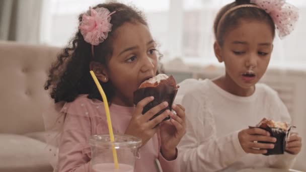 两只可爱的混血小妹 头戴蝴蝶结帽带 坐在家里 吃着美味的纸杯蛋糕 其中的特写镜头 — 图库视频影像