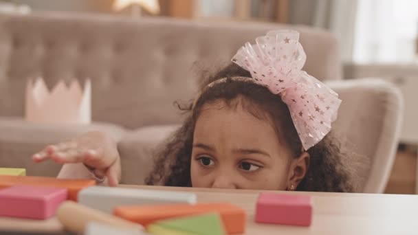 살짜리 소녀가 머리에 두르고 거실에서 테이블에서 웃으며 장난감 나무로 벽돌을 — 비디오