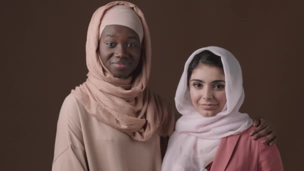 穆斯林男女混血儿和非洲裔美国妇女头戴头巾 头戴头巾 头戴阿拉伯头巾 在褐色背景下站在一起 看着相机的中景肖像画 — 图库视频影像