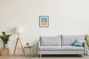 Özet sanat eserleriyle beyaz duvara yaslanmış rahat bir kanepeye odaklanmış minimal ev içi görüntüsü, boşluğu kopyala