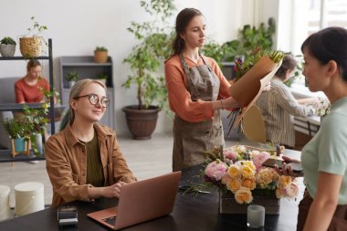 Portrait of two young female florists consulting customers while working in flower shop, copy space